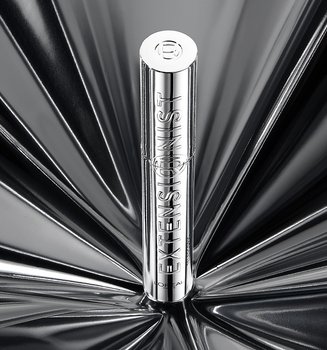 A single silver L'Oréal mascara tube standing upright in the center of a dramatic, reflective silver background with a radial light pattern.