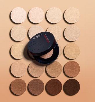 A circular black L'Oréal compact placed in the center of a grid of foundation shade swatches, ranging from very fair to deep brown.